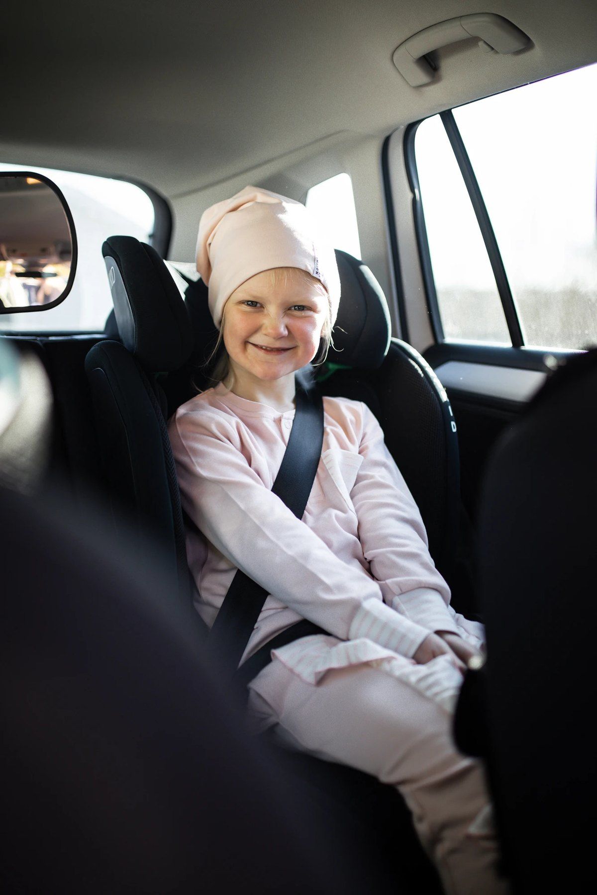 Une fillette souriante assise sur un Axkid Up, ceinture bouclée.