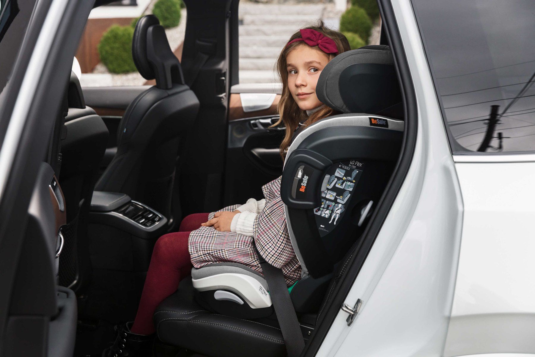 Une fillette assise sur un BeSafe iZi Flex Fix dans une voiture blanche, porte ouverte.