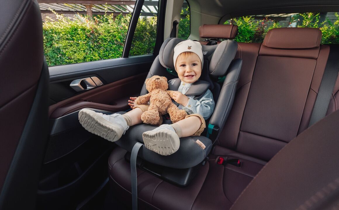 Un tout-petit souriant, attaché par le harnais dans le Advansafix Pro, avec son ours en peluche sur la banquette arrière