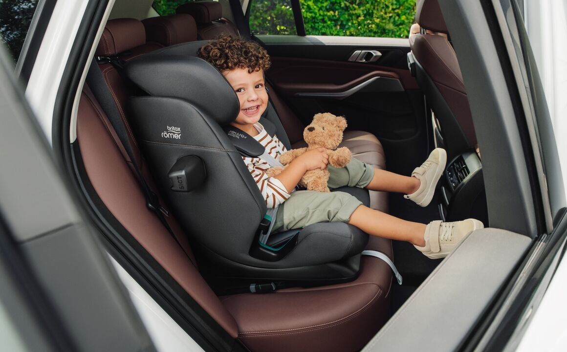 Un enfant assis dans le Advansafix Pro, un ours en peluche sur les genoux, la ceinture de la voiture sur l'épaule