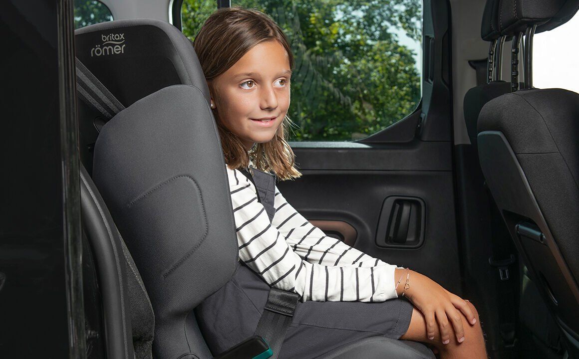 Une fillette en pull rayé assise sur le Adventure Plus 2, la ceinture de la voiture sur son épaule, dans un monospace