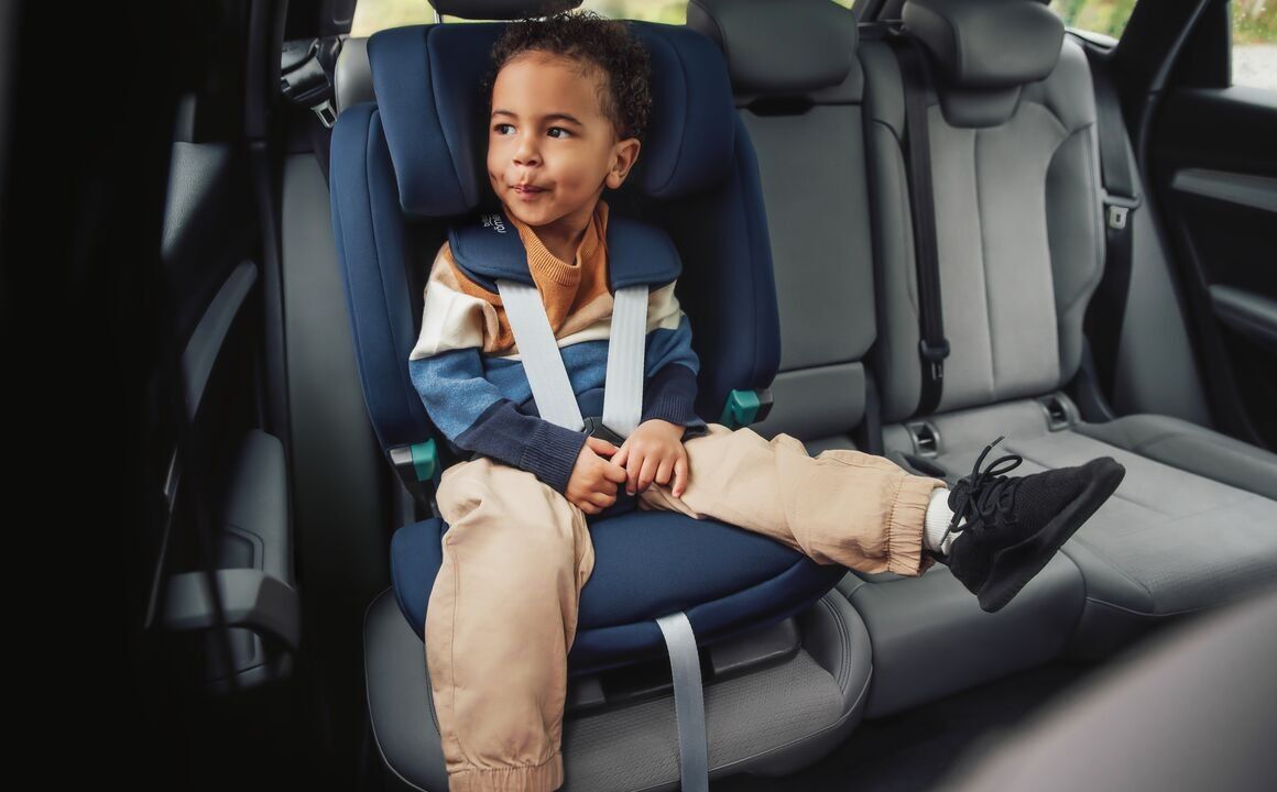 Un garçon assis dans le Evolvafix bleu, la ceinture de la voiture sur l'épaule, à l'arrière d'une voiture