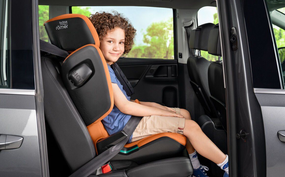Un garçon assis dans le Kidfix i-Size orange, vu de profil, à l'arrière d'une voiture