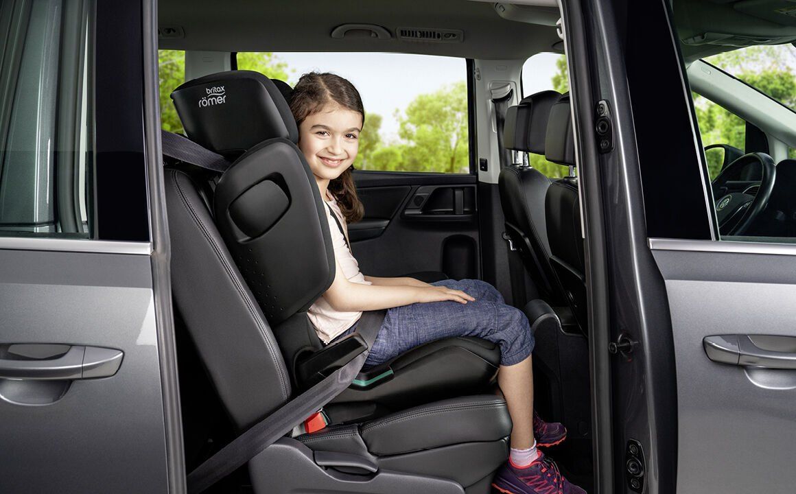Une fillette qui sourit, assise dans le Kidfix Pro M à l'arrière d'une voiture, portière ouverte