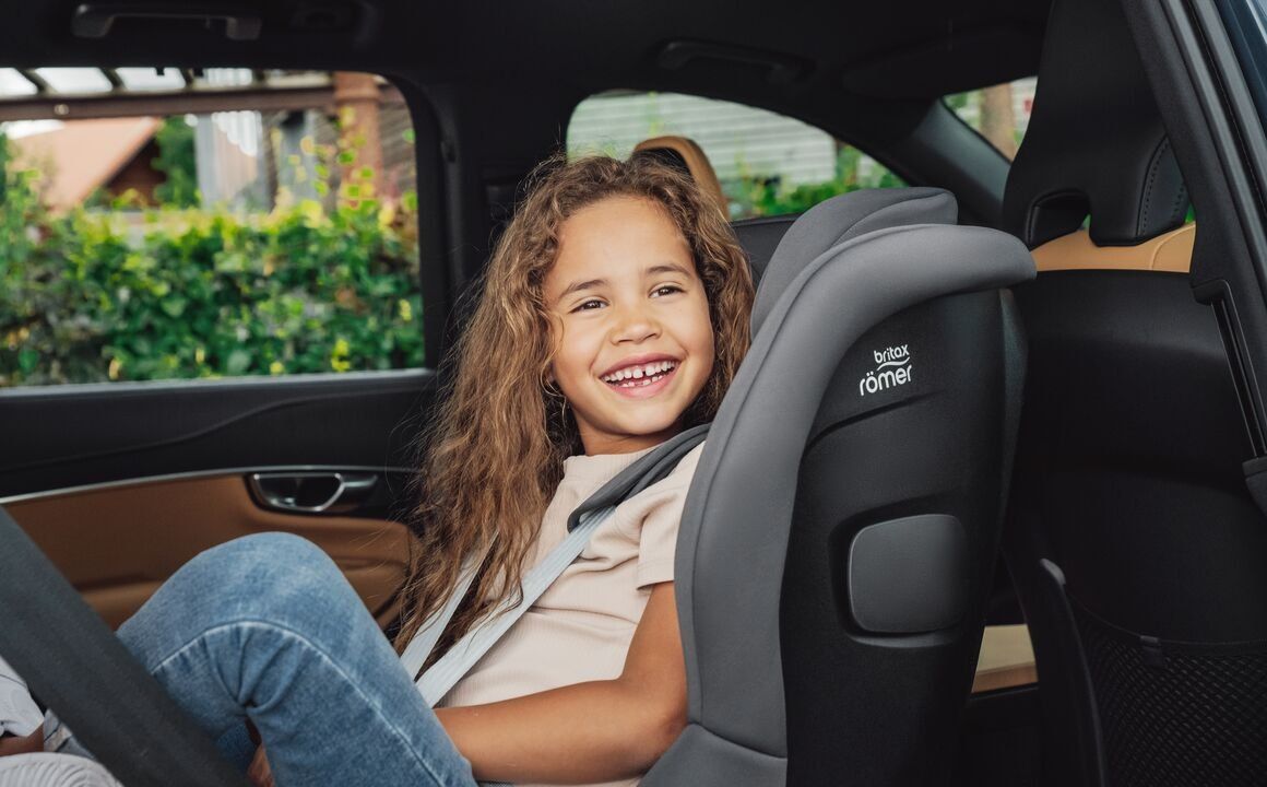 Une fillette qui rit, attachée dans le Safe-Way M, vue de côté à l'arrière d'une voiture