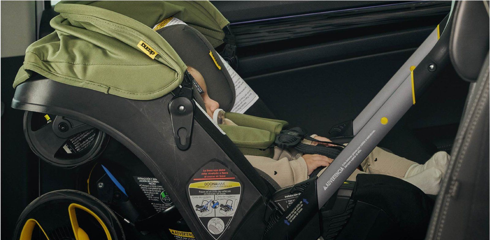Un bébé dans la coque Doona attachée avec la ceinture de la voiture, la sangle passée dans les guides de la coque