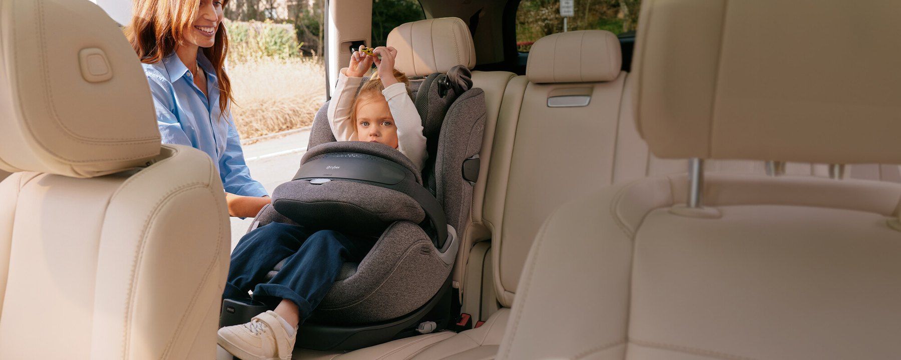 Une maman souriante attache son enfant dans le siège Cybex Anoris T2 i-Size, installé dans une voiture.