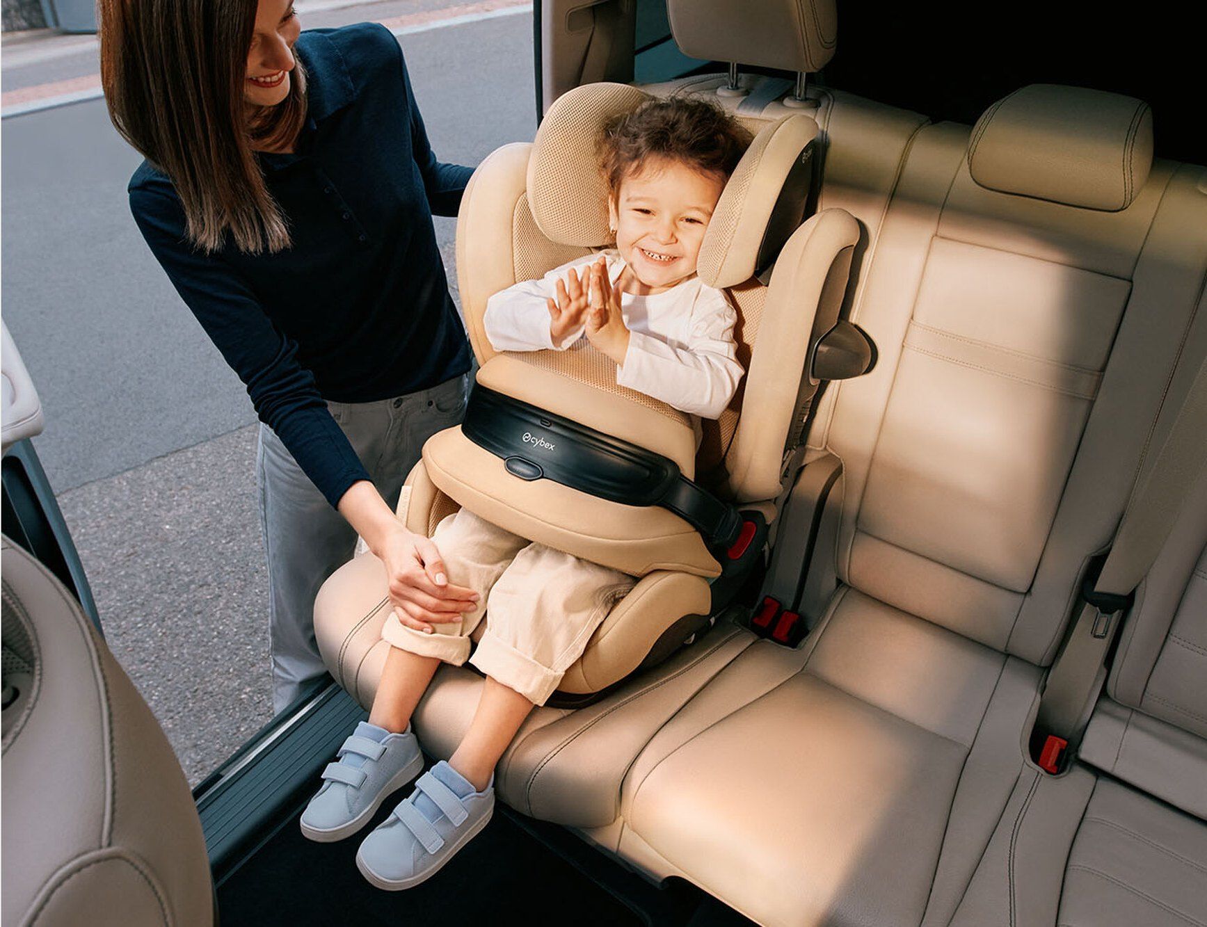 Un enfant souriant assis dans le siège Cybex Pallas G3 sur la banquette arrière, un parent à côté de lui.