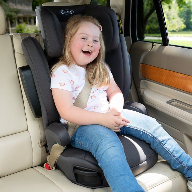 Une petite fille souriante, assise sur le rehausseur EverSure à l'arrière d'une voiture, la ceinture sur l'épaule