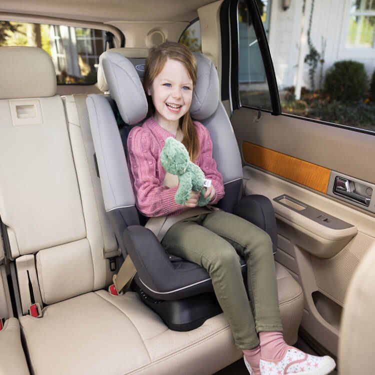 Une fillette souriante avec une peluche, assise dans le siège SlimFit à l'arrière d'une voiture