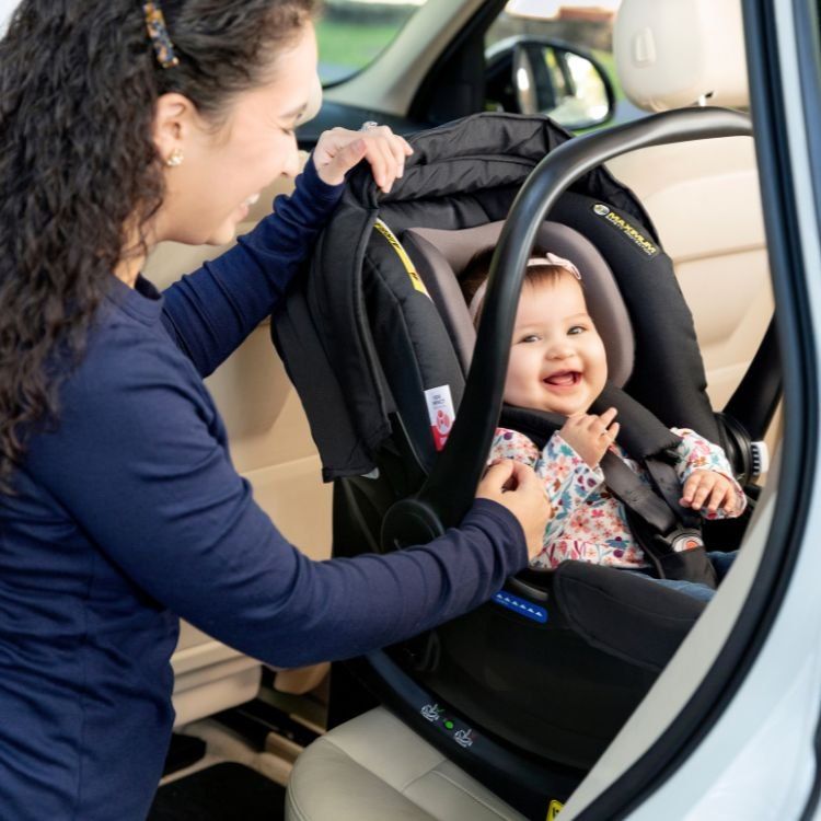 Une maman sourit à son bébé installé dans la coque SnugEssentials, sur la banquette d'une voiture