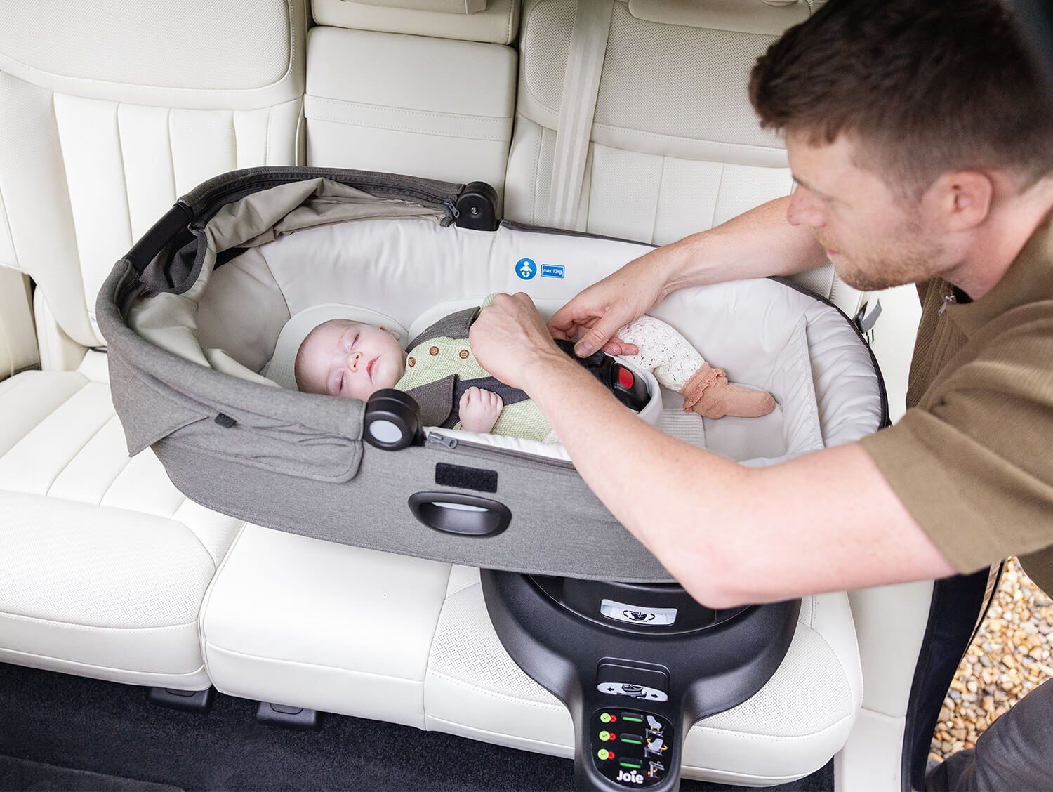 Un père attache un bébé allongé dans la nacelle Joie Calmi installée sur la banquette arrière