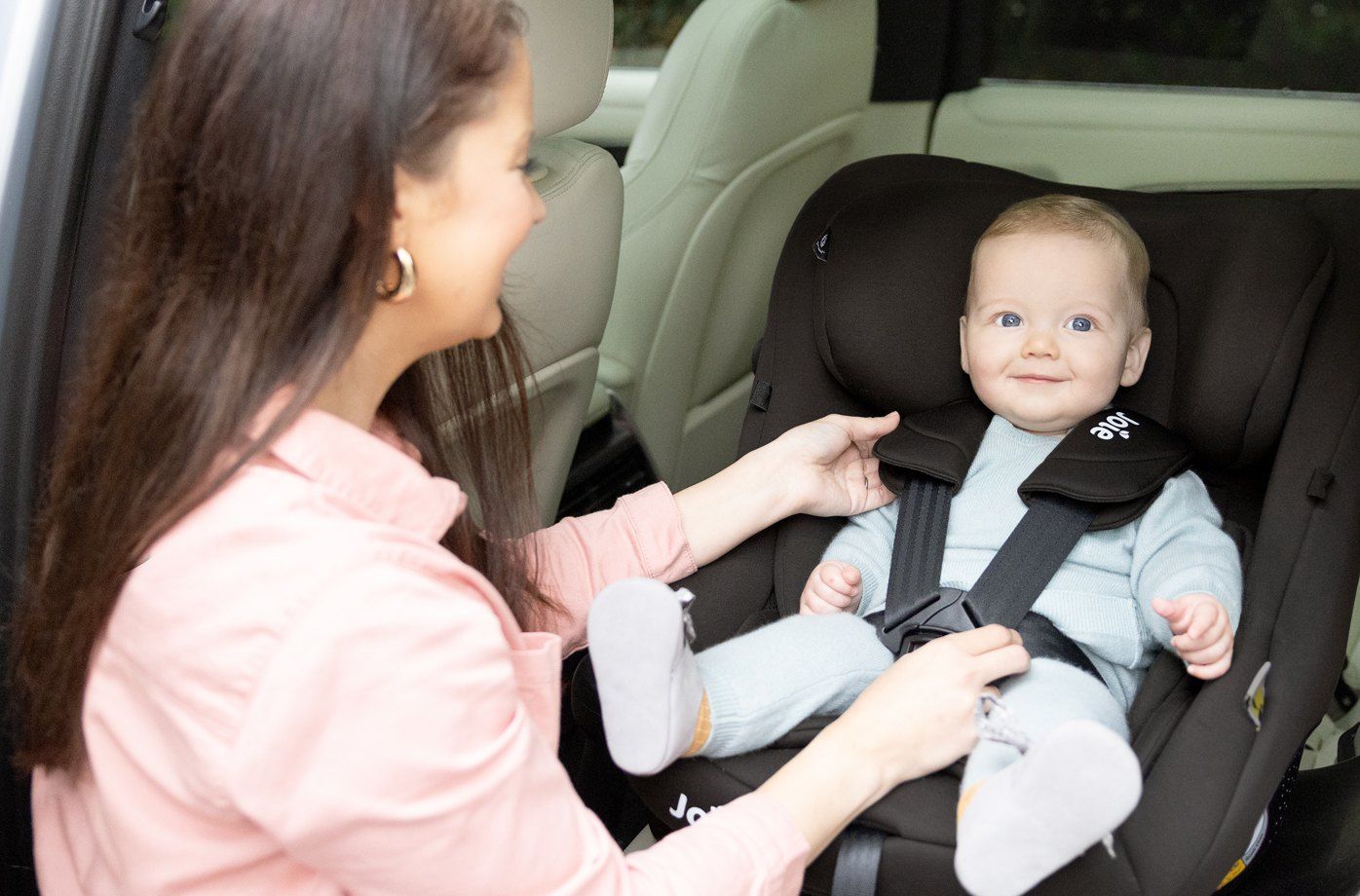 Une maman attache un bébé souriant dans un siège Joie i-Pivot 360 en voiture