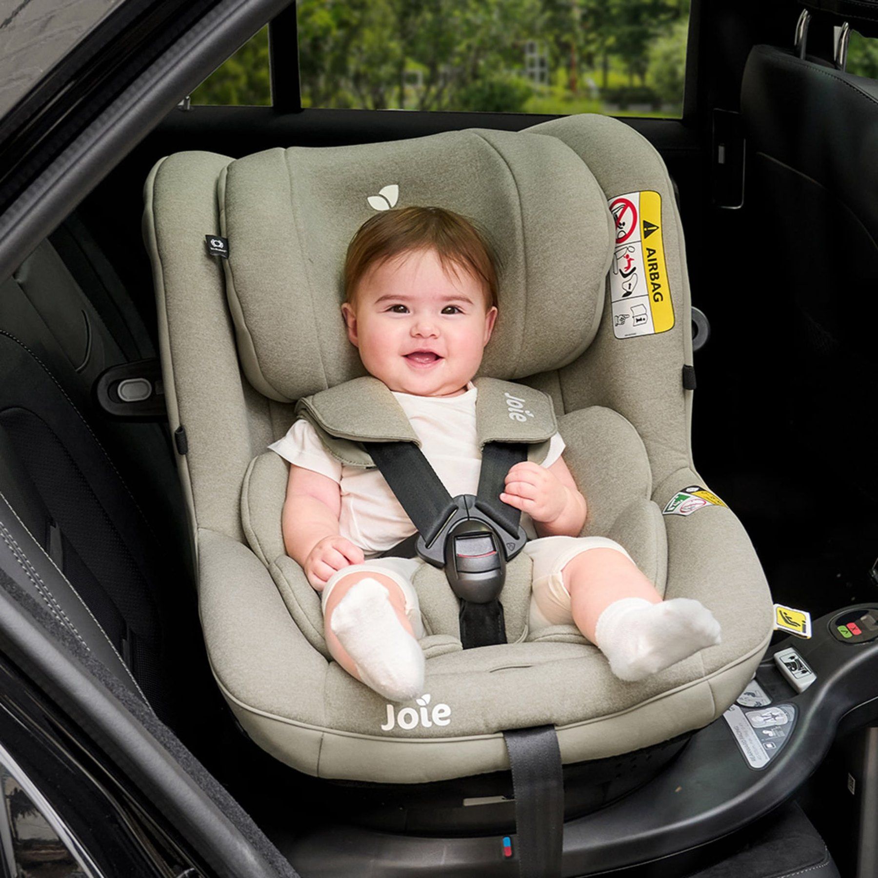 Un bébé souriant attaché dans un i-Spin 360 vert sauge, installé sur la banquette d'une voiture.