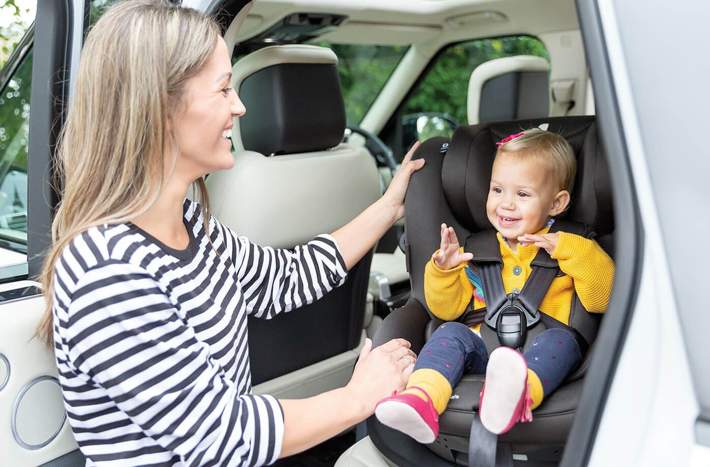 Une maman aide un bébé souriant dans un siège Joie i-Spin Safe installé en voiture