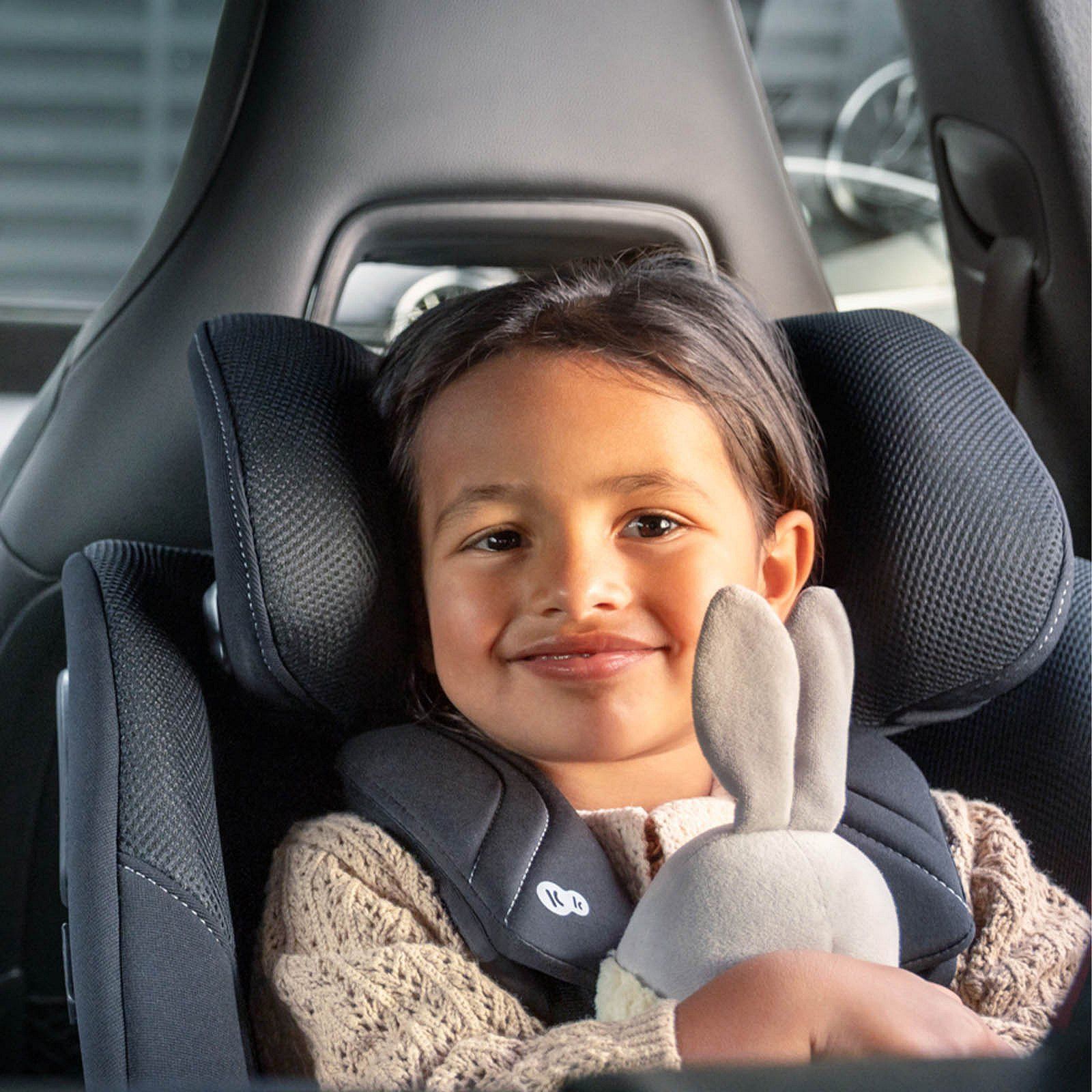 Une petite fille souriante, un doudou dans les bras, attachée dans le siège Kinderkraft i-Guard Pro.