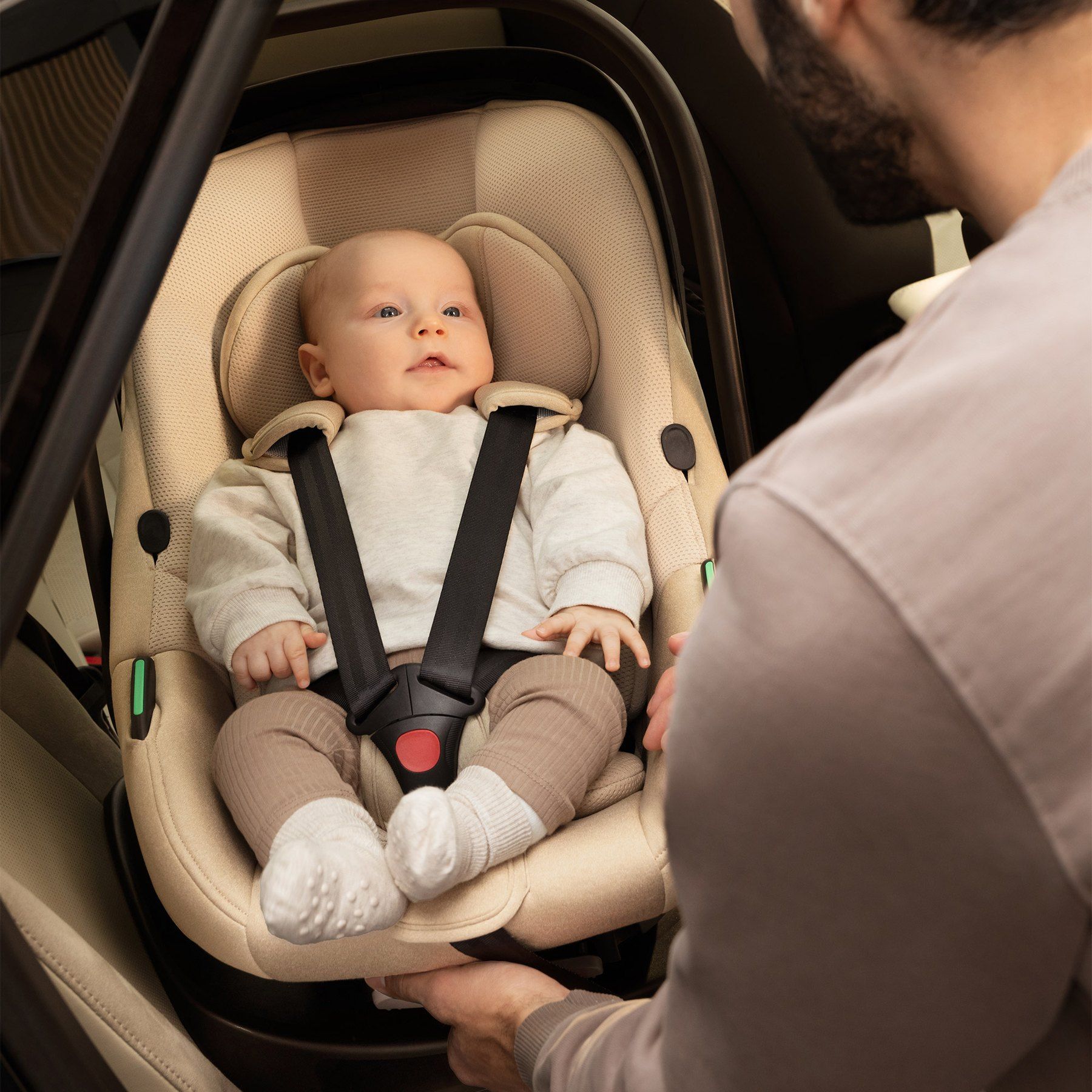 Un papa règle le harnais de son bébé, installé dans la coque Kinderkraft I-Lite à l'arrière d'une voiture.