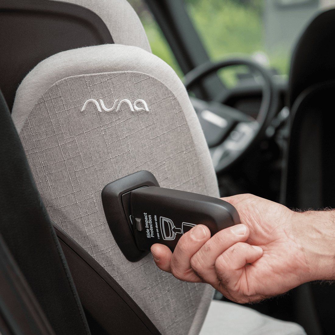 Main qui actionne la protection latérale à l'arrière du dossier du rehausseur Nuna Aace LX, dans une voiture.
