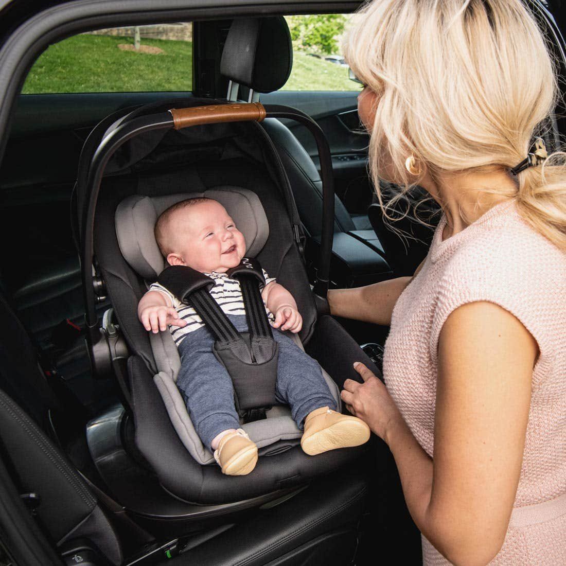 Une maman installe son bébé souriant dans la coque Nuna Arra Next, à l'arrière d'une voiture.