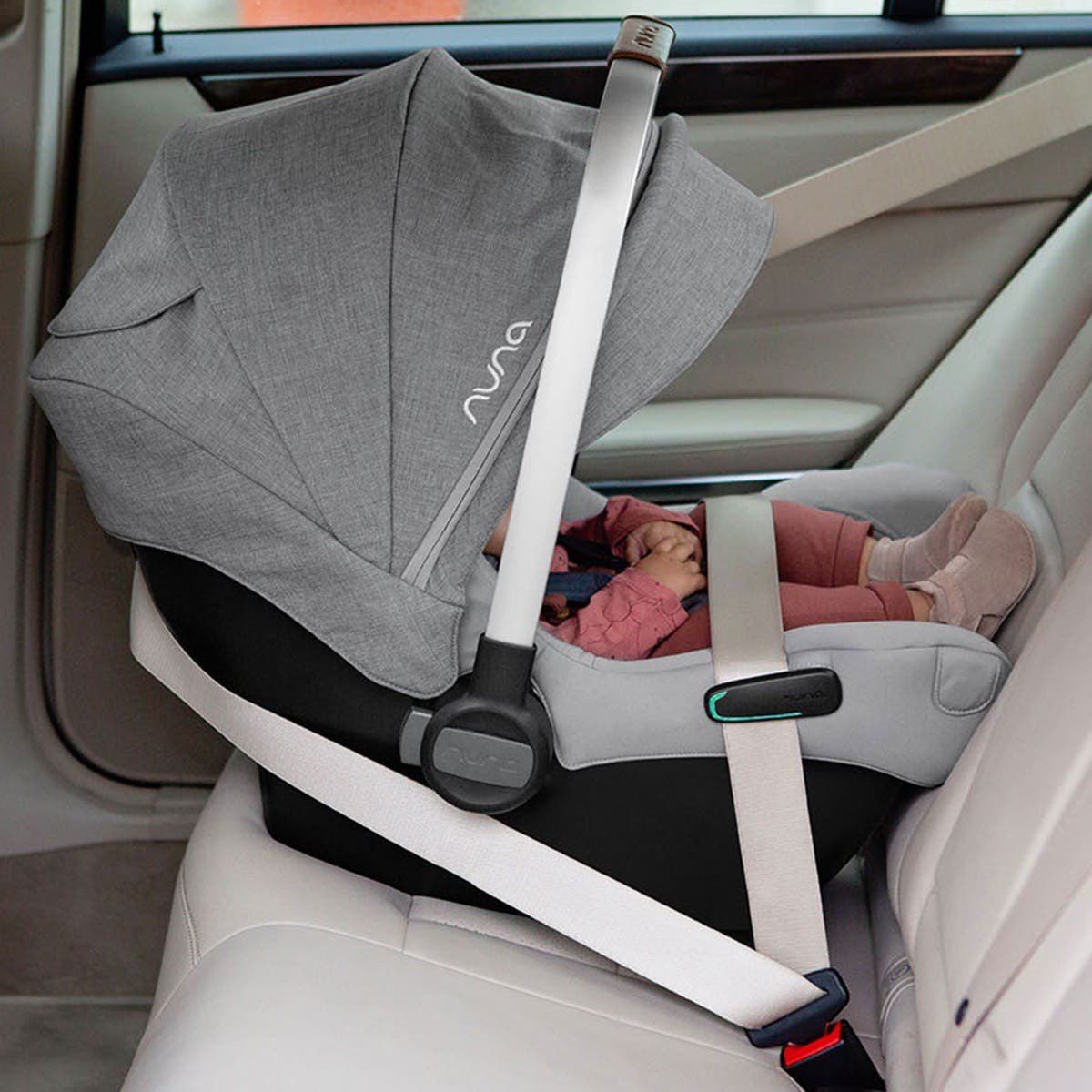 Coque bébé Nuna Pipa Next fixée avec la ceinture de sécurité sur une banquette, un bébé allongé à l'intérieur.