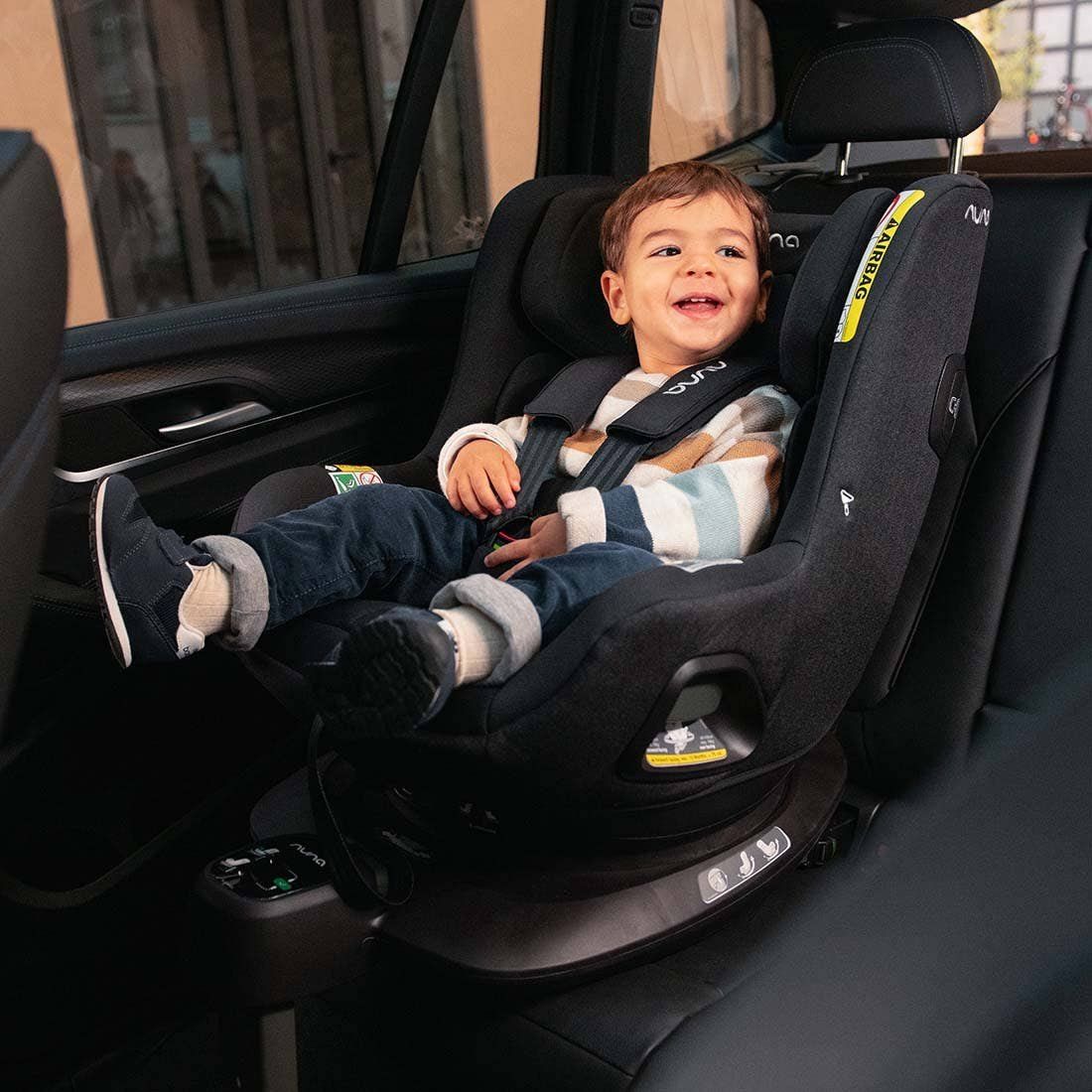 Un petit garçon souriant installé dans le siège Nuna Pruu, face à la route, sur la banquette arrière.