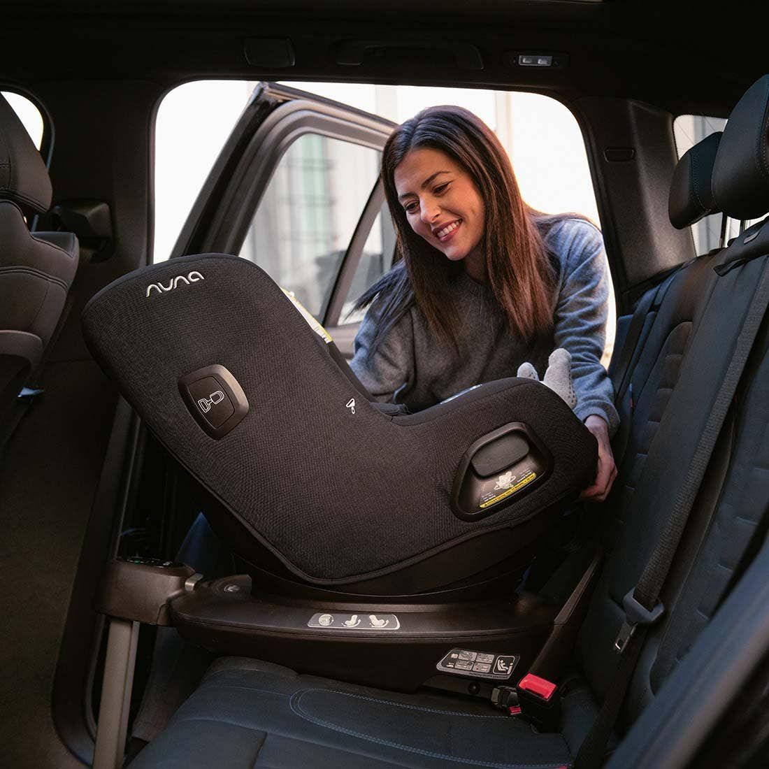 Une maman souriante pivote le siège Nuna Pruu à côté de la portière ouverte d'une voiture.