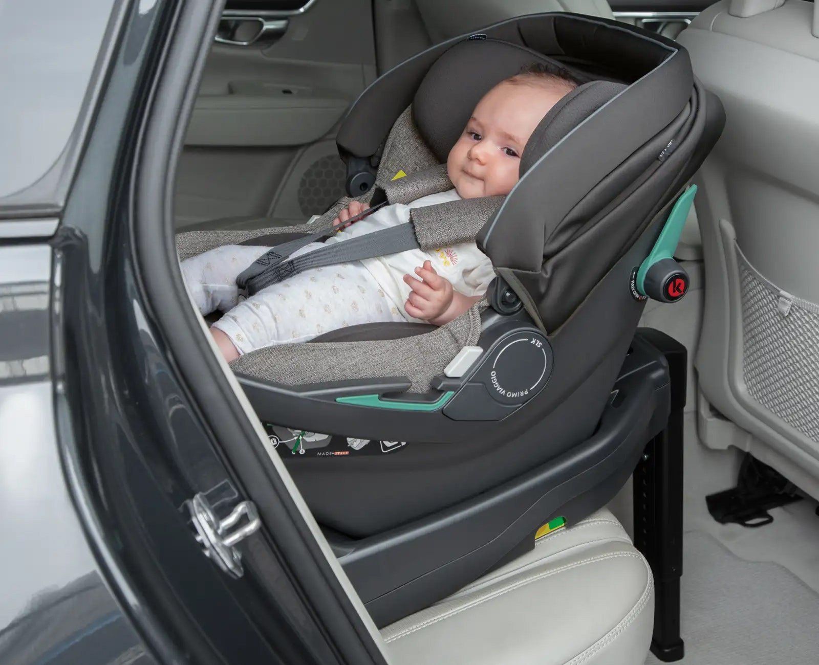 Un nouveau-né installé dans la coque Primo Viaggio SLK sur sa base, dans une voiture, porte ouverte.