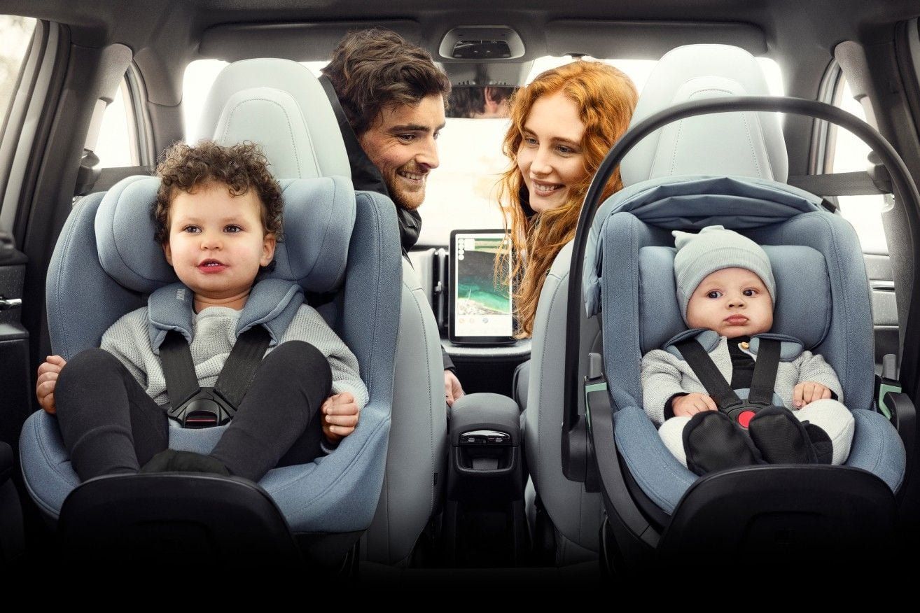 Un couple se retourne depuis les sièges avant vers ses deux enfants installés à l'arrière, l'aîné dans un siège auto Thule et le bébé dans une coque Thule