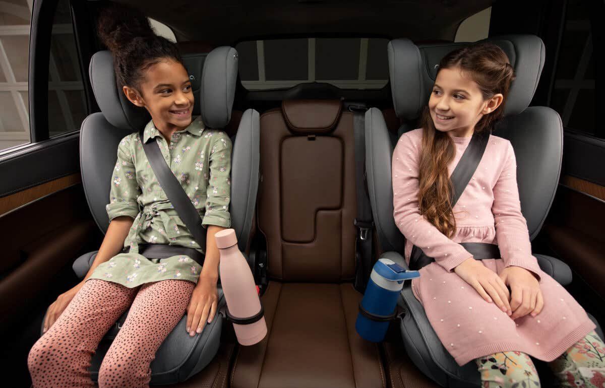 Deux fillettes assises de part et d'autre de la banquette arrière, chacune sur un rehausseur à dossier Nuna avec la ceinture de la voiture