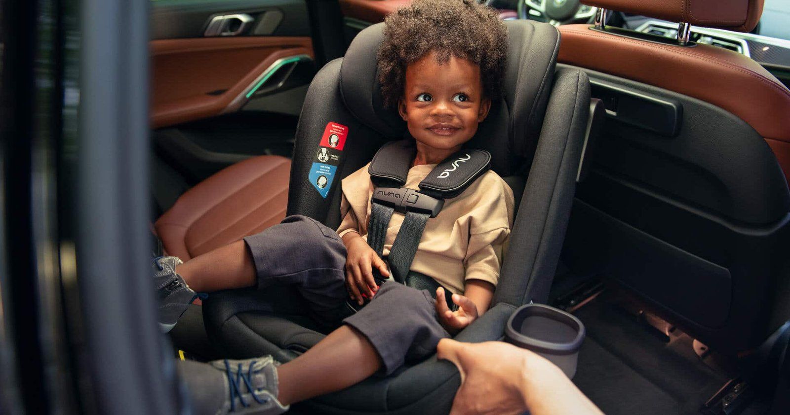 Un petit garçon souriant attaché par le harnais dans un siège auto Nuna face à la route, à l'arrière d'une voiture
