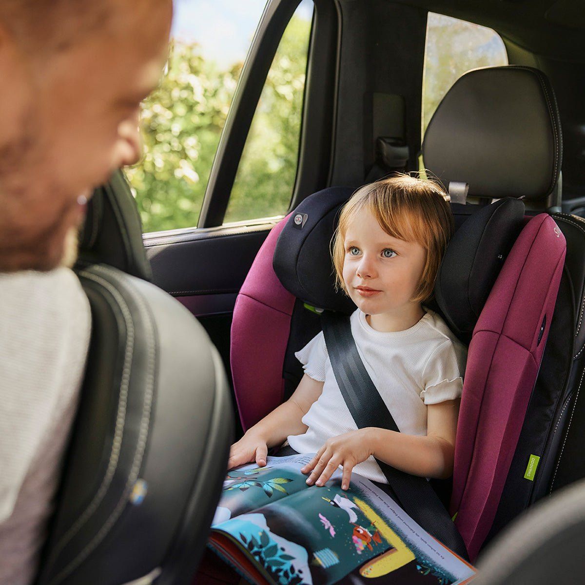 Une petite fille attachée sur un Swandoo Charlie prune, un livre sur les genoux.