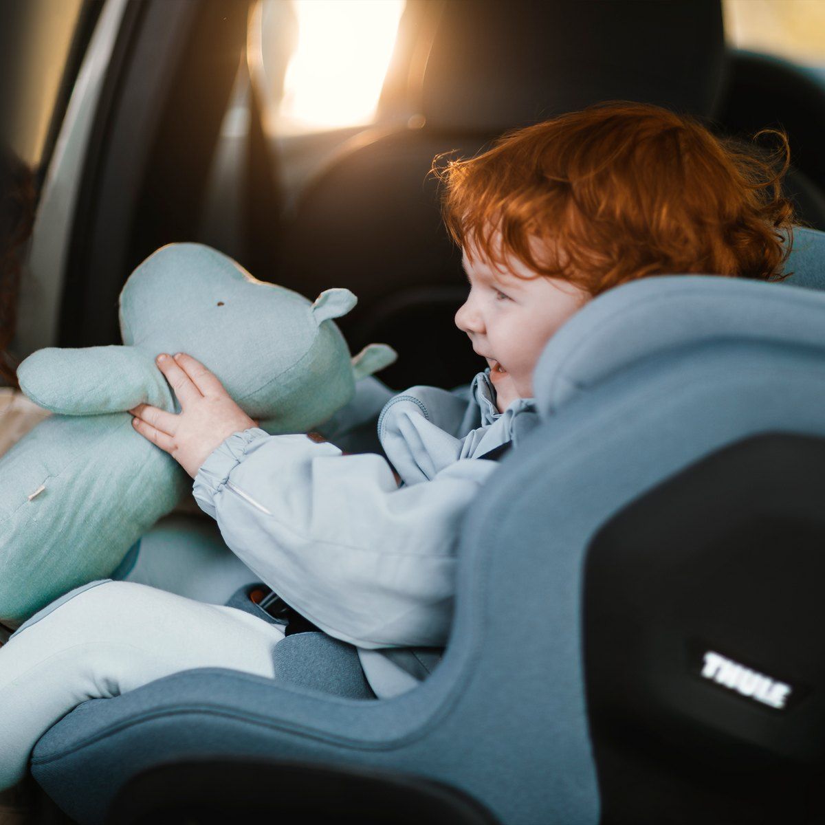 Un enfant aux cheveux roux qui serre une peluche, assis dans le Thule Elm