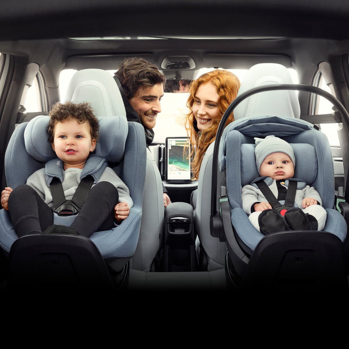 Une famille dans une voiture, un tout-petit assis dans un siège Thule et un bébé dans sa coque, avec leurs parents qui les regardent