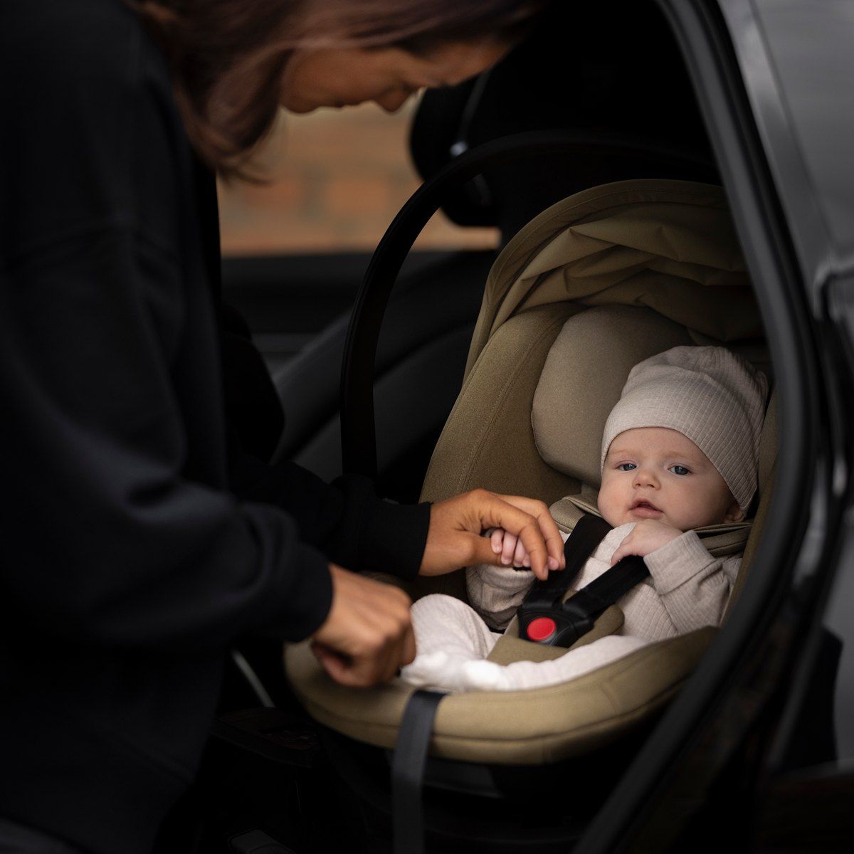 Une maman qui attache un bébé dans la coque Thule Maple, installée à l'arrière d'une voiture