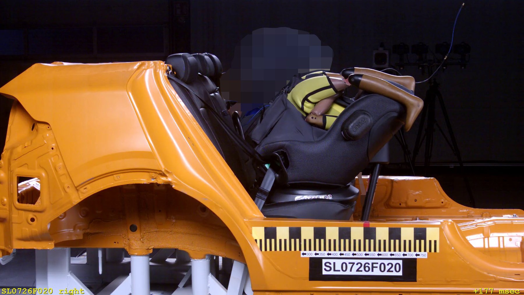Le Minikid Core d'Axkid installé dos à la route sur la caisse orange de crash-test de l'ADAC, pendant la collision frontale, un mannequin à l'intérieur