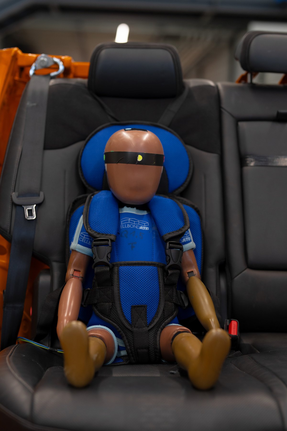 Un mannequin de crash-test attaché par des sangles dans un siège souple bleu sans marque